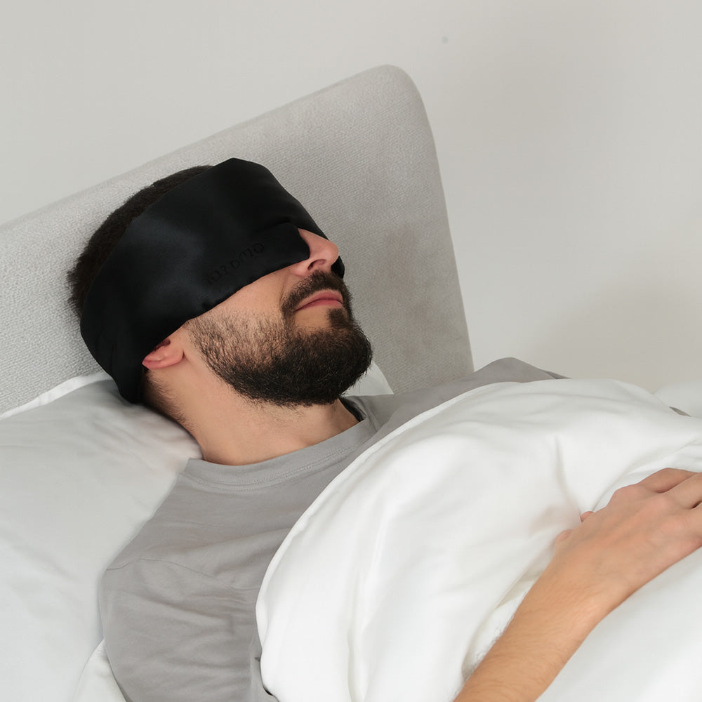 Man wearing a black silk sleep mask in bed