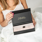 Person holding a black box with text and a brand logo, sitting on a white surface.