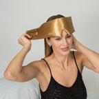 Woman wearing a gold silk sleep mask with a plain background