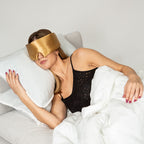 Woman wearing a gold silk sleep mask with a plain background