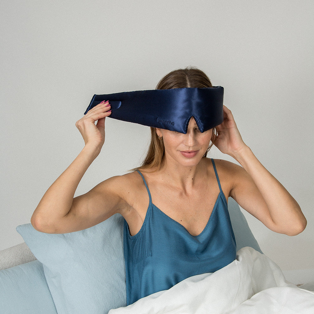 Woman wearing a blue silk eye mask in bed