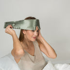 Woman wearing a green silk eye mask with a plain background