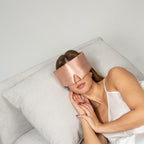 Woman wearing a rose gold silk sleep mask against a plain background
