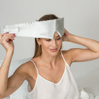 Woman wearing a silver silk sleep mask with a plain background