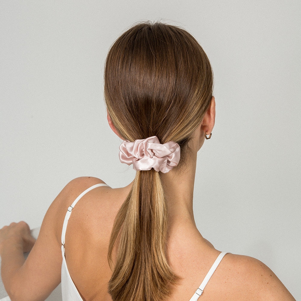 Woman with a pink scrunchie in her ponytail against a plain background
