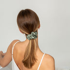 Woman with a ponytail held by a green scrunchie against a plain background