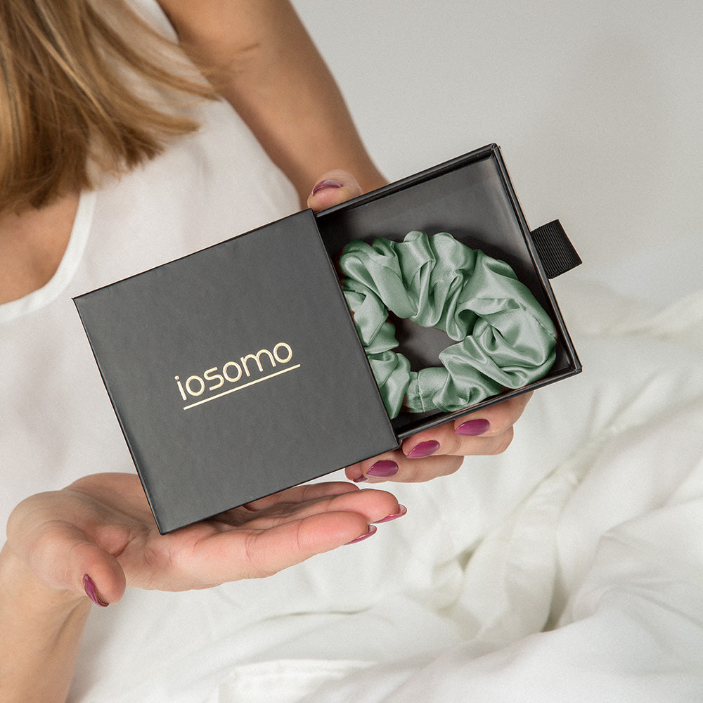 Person holding a green scrunchie in an 'iosomo' branded box.
