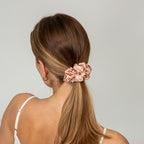 Woman with a ponytail held by a pink scrunchie against a plain background