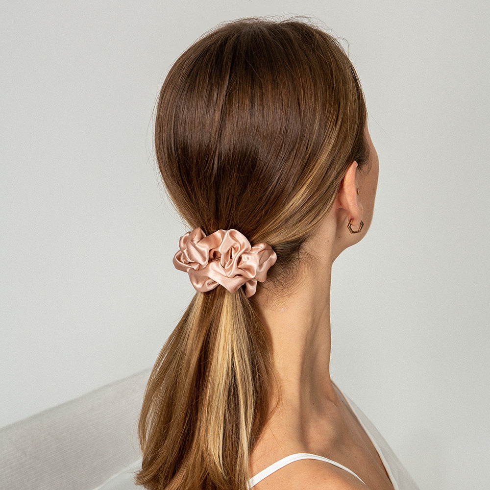 Woman with a ponytail held by a pink scrunchie against a neutral background