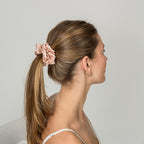 Woman with a high ponytail wearing a pink scrunchie against a plain background